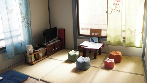 A traditional Japanese room with tatami flooring, a television, a desk, and a window with floral curtains. - Oyado Ichigo Nisho 27 IG1 (Ito)
