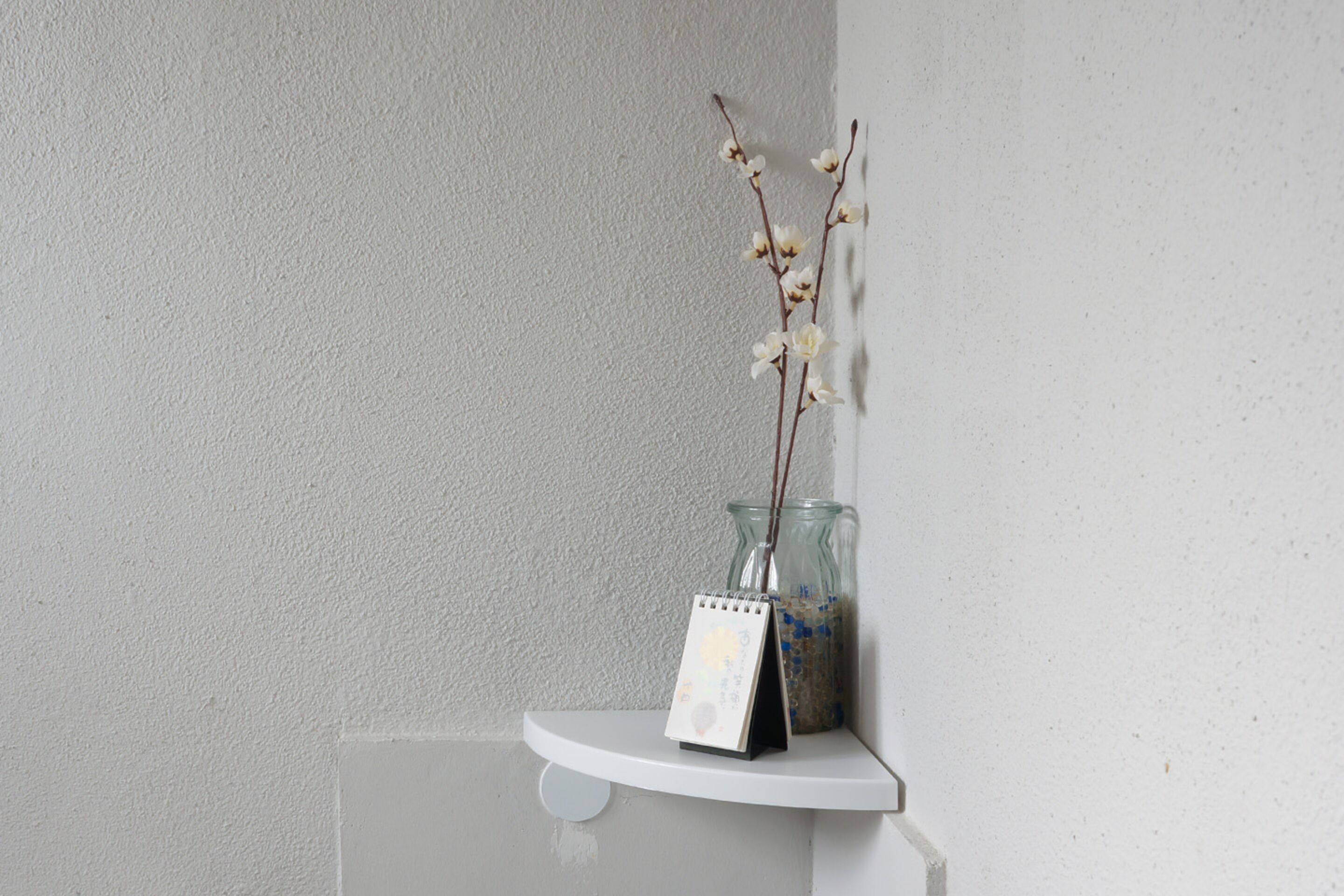 Una estantería blanca con un calendario y un florero con ramas.