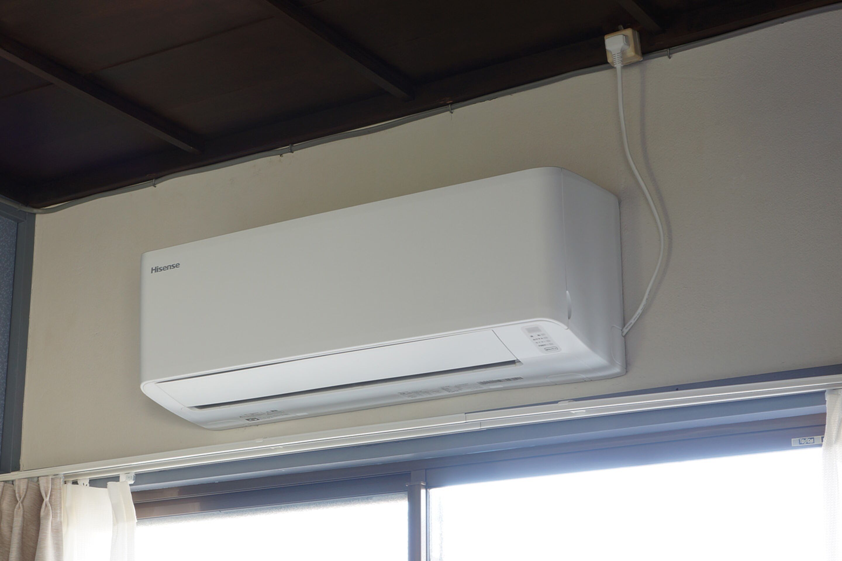 A white Hisense air conditioner mounted on a wall above a window with a curtain.
