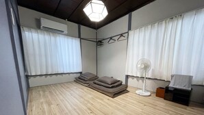 A room with wooden flooring, a bed with pillows, a standing fan, and an air conditioning unit. - Oyado Ichigo Nisho 27 IG1 (Ito)