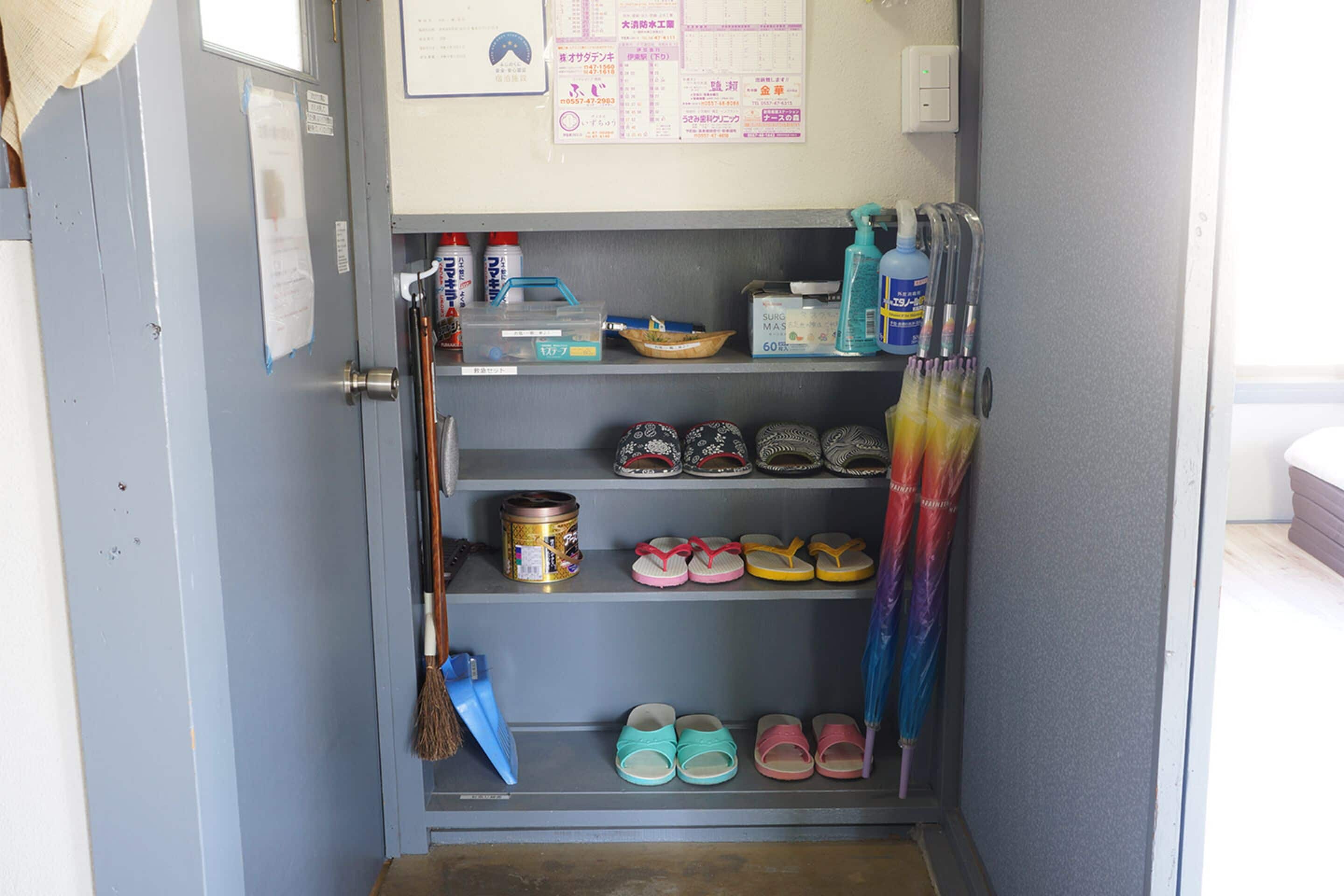 Un módulo de almacenamiento con estanterías que contienen varios objetos, incluyendo zapatos, productos de limpieza y una escoba.