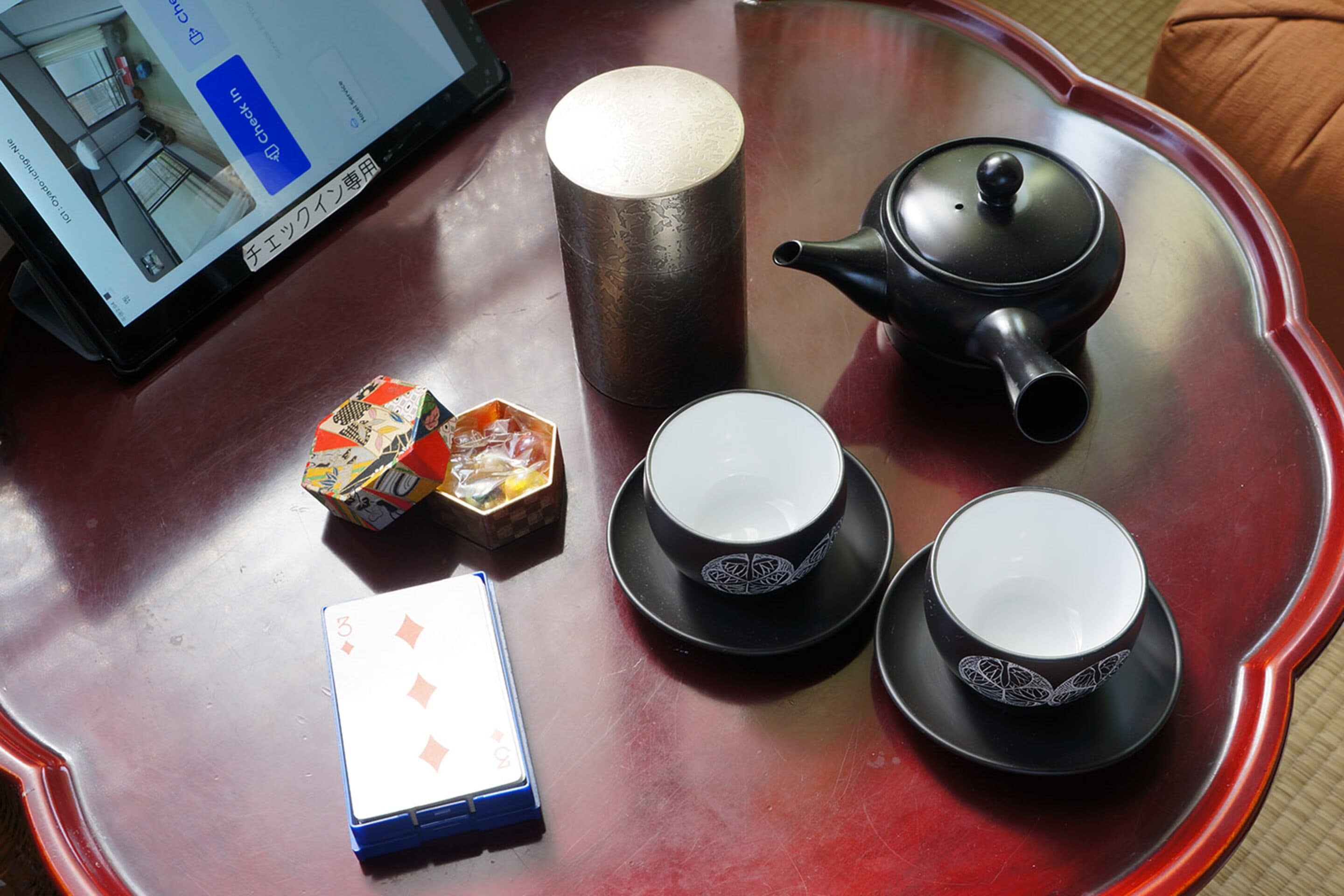 A table with a teapot, two cups, a box of tissues, and a playing card.