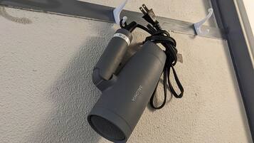 A black device with a cord and a plug, mounted on a textured wall with two white hooks.