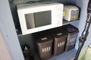 A microwave oven, a toaster, and two trash bins with a broom in a utility area.