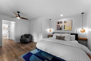 Une chambre avec un grand lit, un ventilateur de plafond, deux lampes fixées au mur et un plancher en bois.