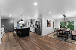 Une cuisine moderne dotée d’un îlot central, d’appareils électroménagers en acier inoxydable et de luminaires suspendus.