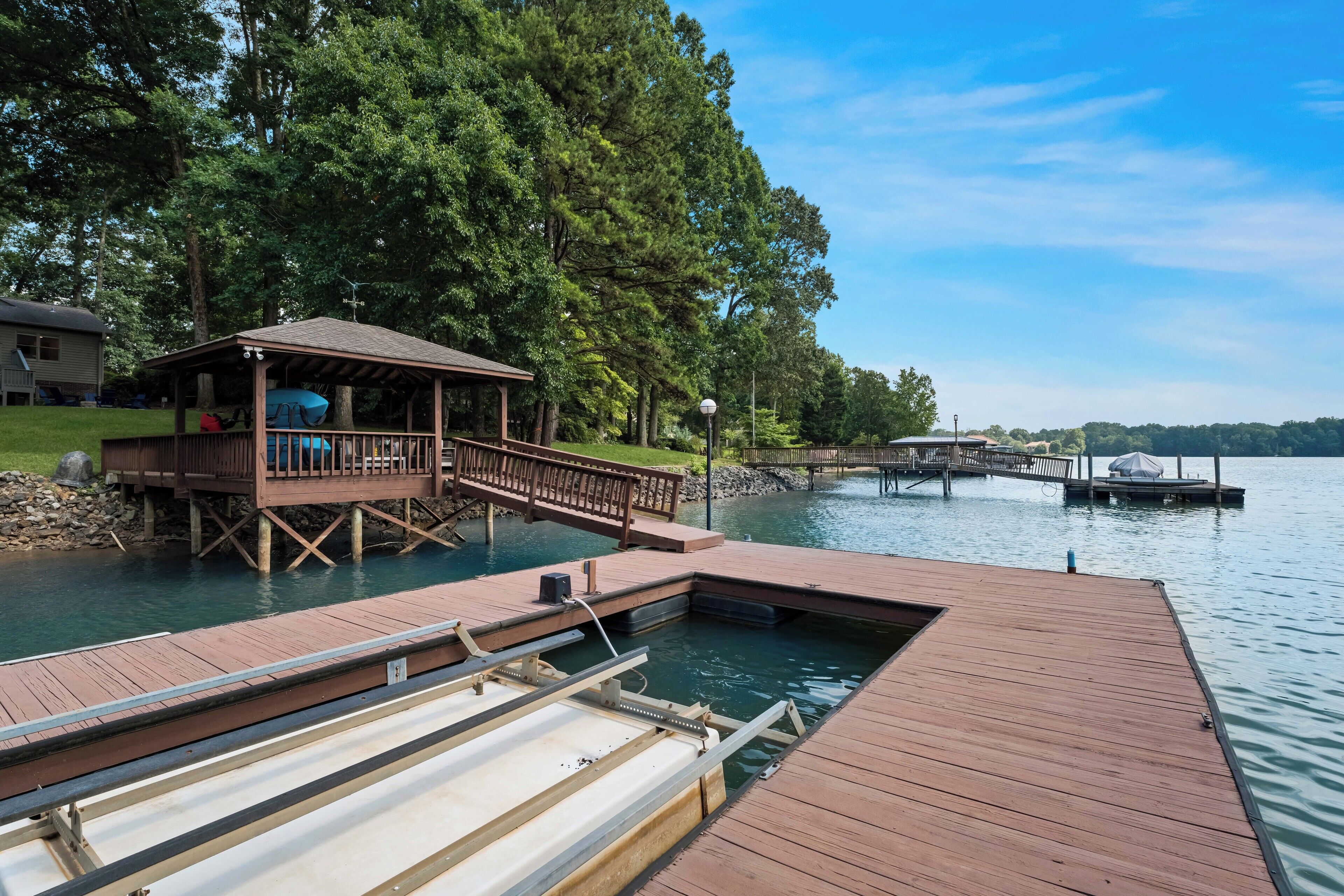A wooden dock extending into a lake, with a covered seating area and a small pavilion.