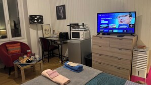 A compact hotel room with a kitchenette, a television displaying a program, a desk with a computer, and a bed with towels. - Studio 1 min walk from Châteaubriant castle with complimentary breakfast (Châteaubriant)