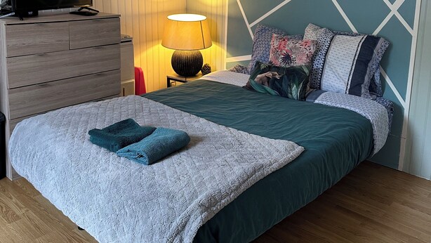 A bedroom with a bed, a TV on a dresser, a lamp, and a geometric headboard. - Studio 1 min walk from Châteaubriant castle with complimentary breakfast (Châteaubriant)
