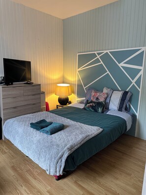 Une chambre à coucher avec un lit, un téléviseur posé sur une commode, une lampe et une tête de lit à motifs géométriques.