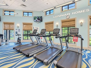 A gym with treadmills, exercise bikes, and a television screen.