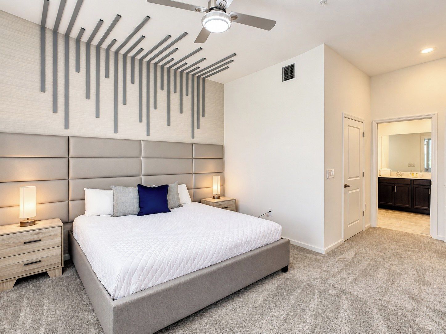 Une chambre à coucher moderne avec un grand lit, des tables de chevet, un ventilateur de plafond et une vue sur la salle de bain.