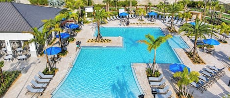 A large swimming pool surrounded by lounge chairs and umbrellas, with a view of apartment buildings in the background.