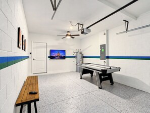 A pool table with a cue stick, a television mounted on the wall, and a ceiling fan.