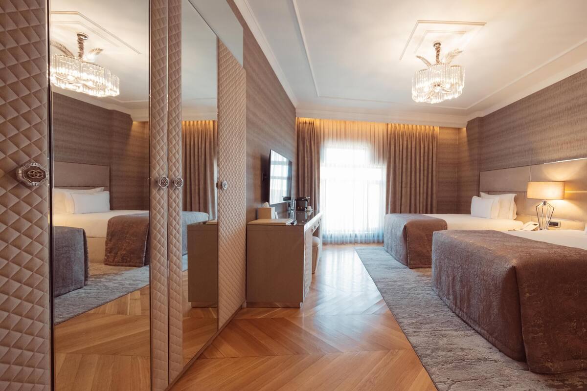 A hotel room with two beds, a desk, a mirror, and a chandelier.