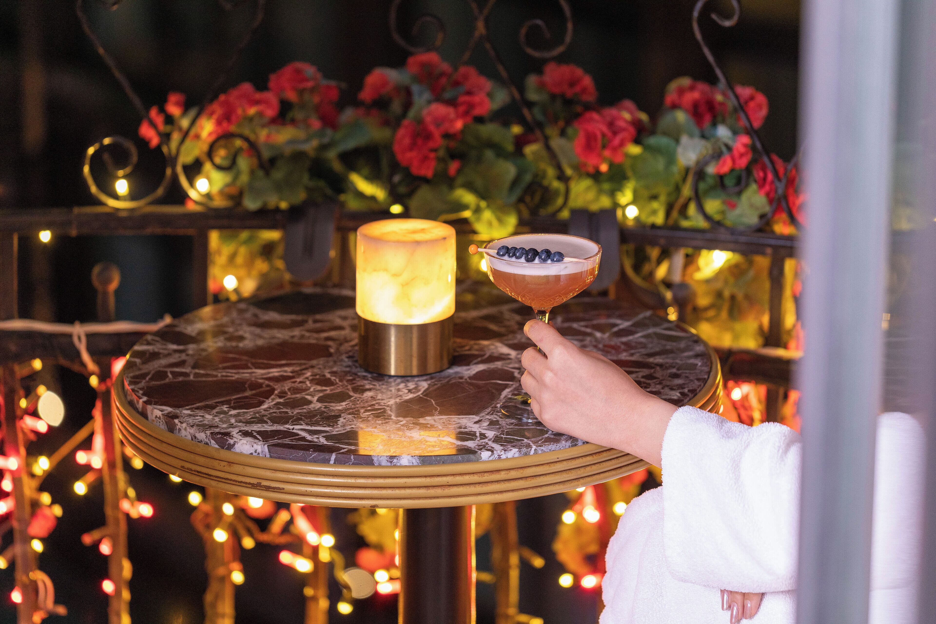 A round table with a marble top, a lit candle, and a cocktail glass with a garnish.
