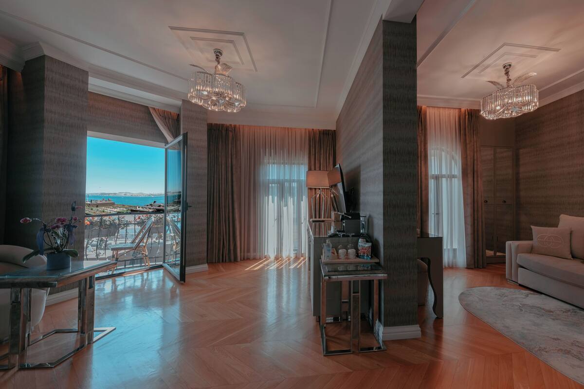 A spacious living room with a large window offering a view of the sea, a modern chandelier, and a cozy seating area.