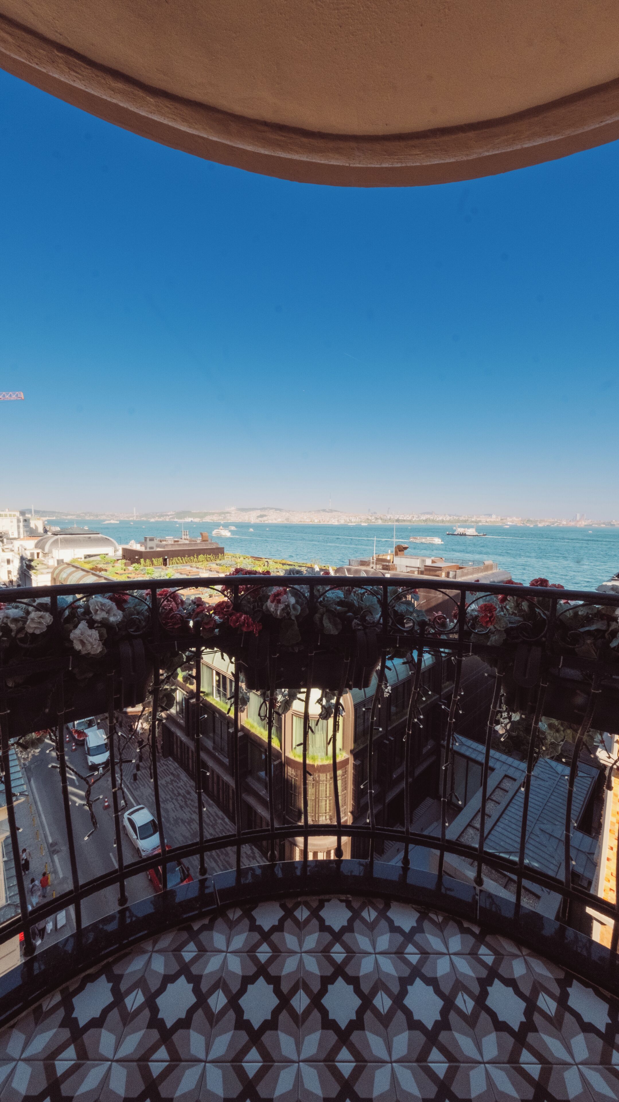 Un balcón con piso estampado, vista al mar y un paisaje urbano de fondo.