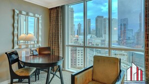 A hotel room with a large window offering a city view, a round table with chairs, a lamp, and a mirror. - 11th Floor Luxurious Suite | Strip & F1 Views (Las Vegas)