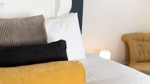 Una cama con ropa blanca, una almohada negra, una almohada marrón y una almohada amarilla.