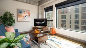 Un salon moderne avec une grande fenêtre, un téléviseur à écran plat, un canapé, une table basse et une plante en pot.