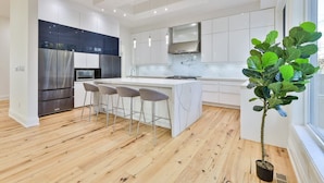 Uma cozinha moderna com ilha central, banquetas, eletrodomésticos de aço inoxidável e uma janela grande.