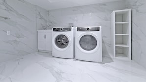 Uma lavanderia moderna com duas máquinas de lavar de abertura frontal, um armário branco e piso de mármore.