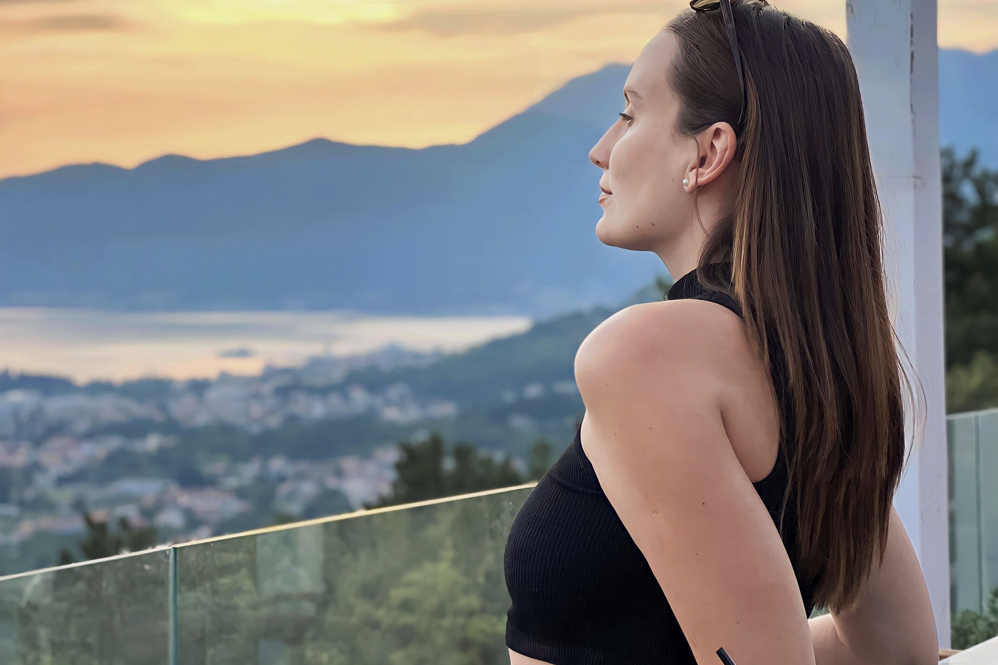 Une personne se tient près d’un balcon, d’où l’on peut admirer une vue sur la ville et les montagnes.