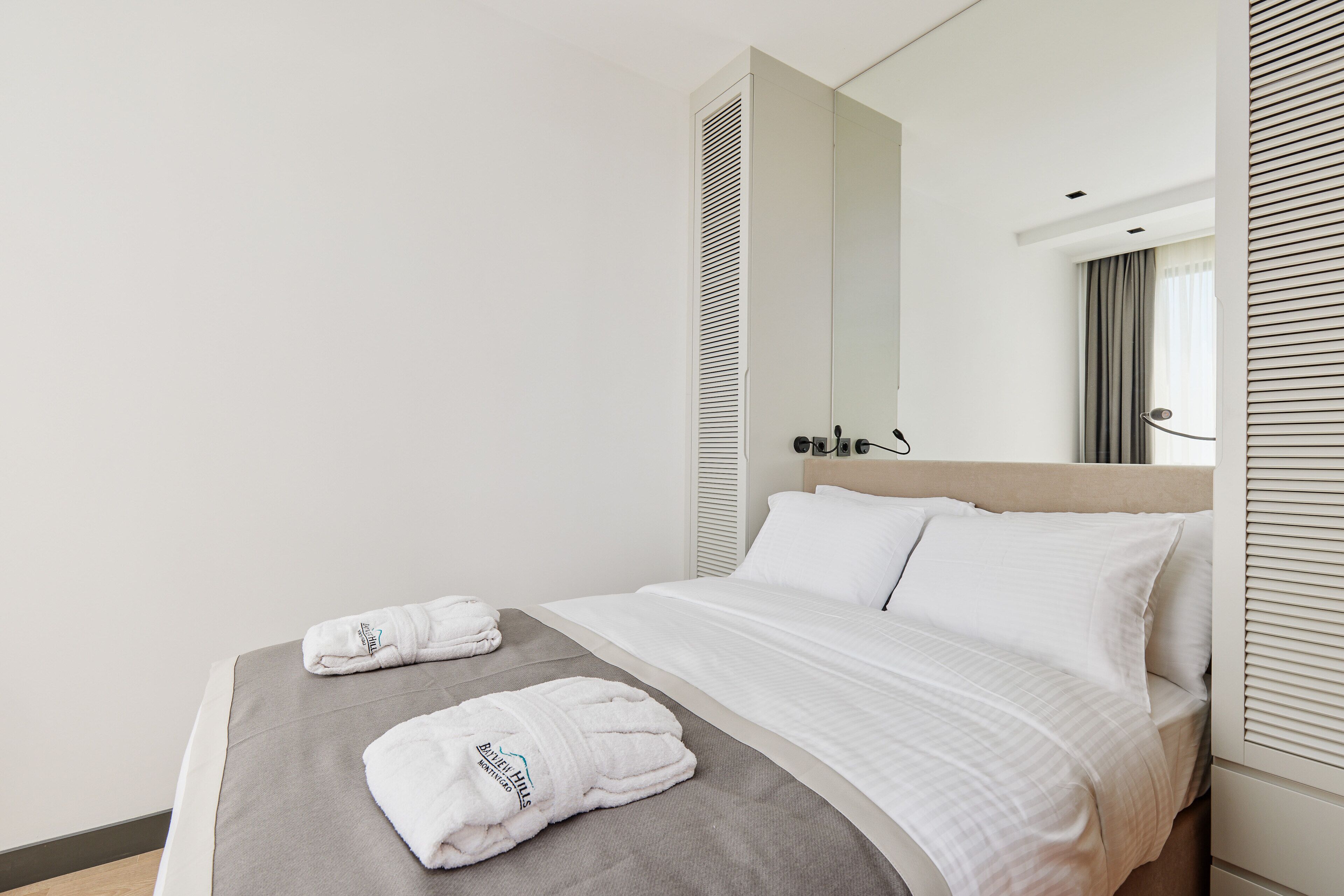 A hotel room with a bed, two towels, a mirror, and a window with blinds.