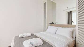 A hotel room with a bed, two towels, a mirror, and a window with blinds.
