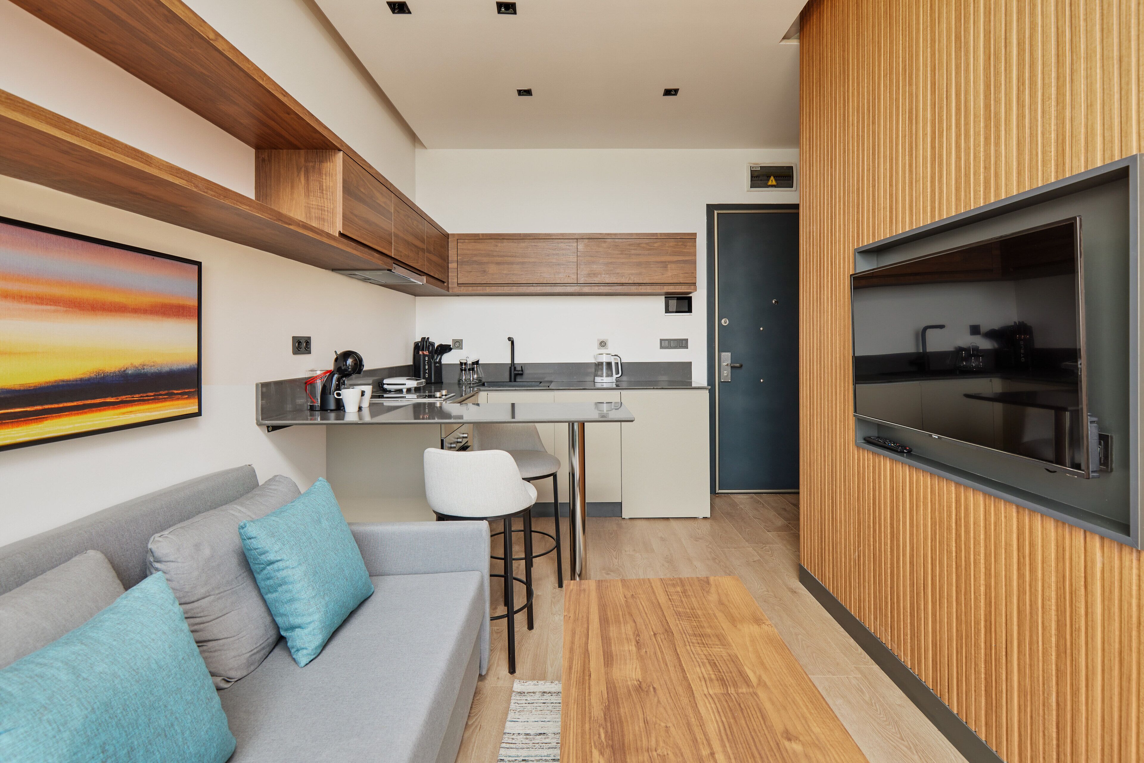 Una cocina moderna con estufa integrada, un rincón comedor con sofá gris y cojines azules, y un amplio ventanal con vistas al espacio.