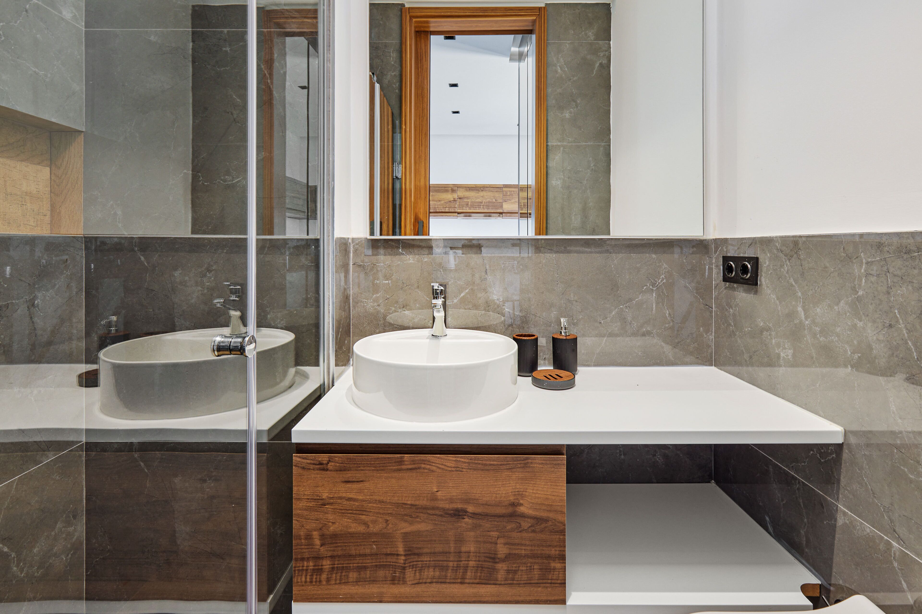A modern bathroom with two sinks, a wooden cabinet, and a mirror.
