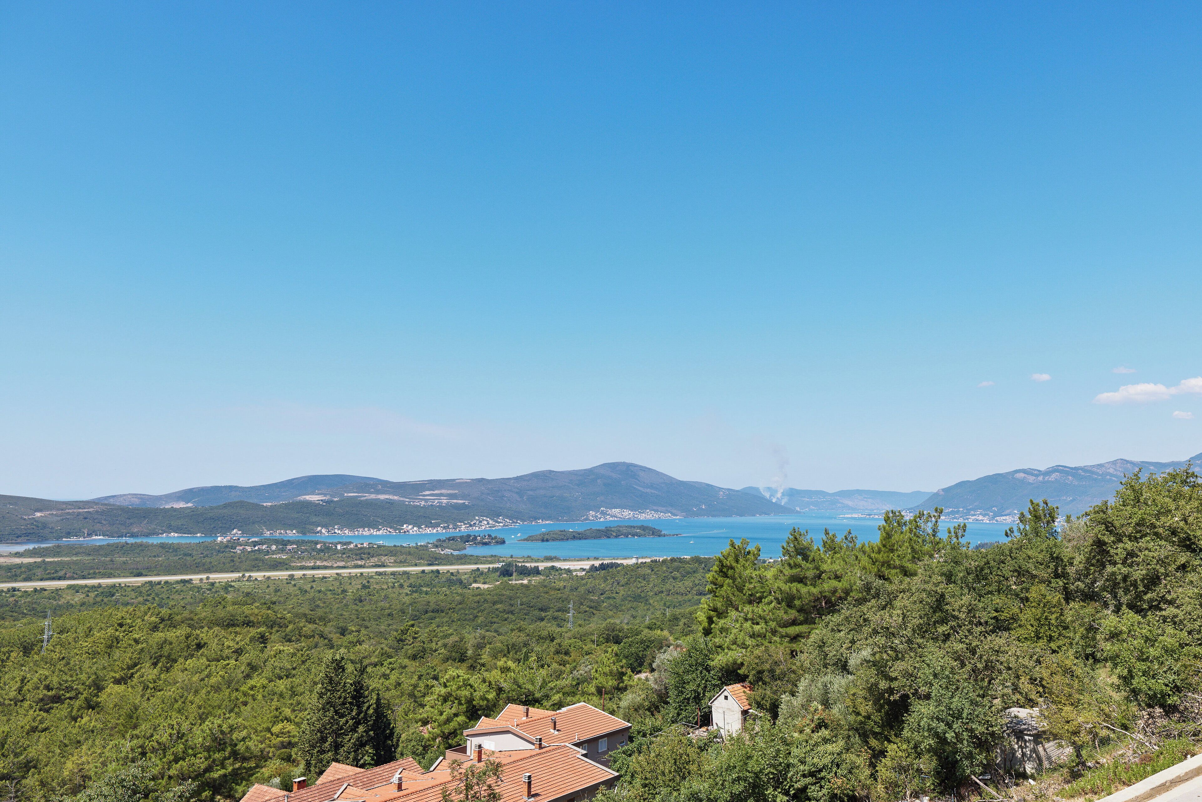 A coastal landscape with houses, dense greenery, and a clear blue sky.