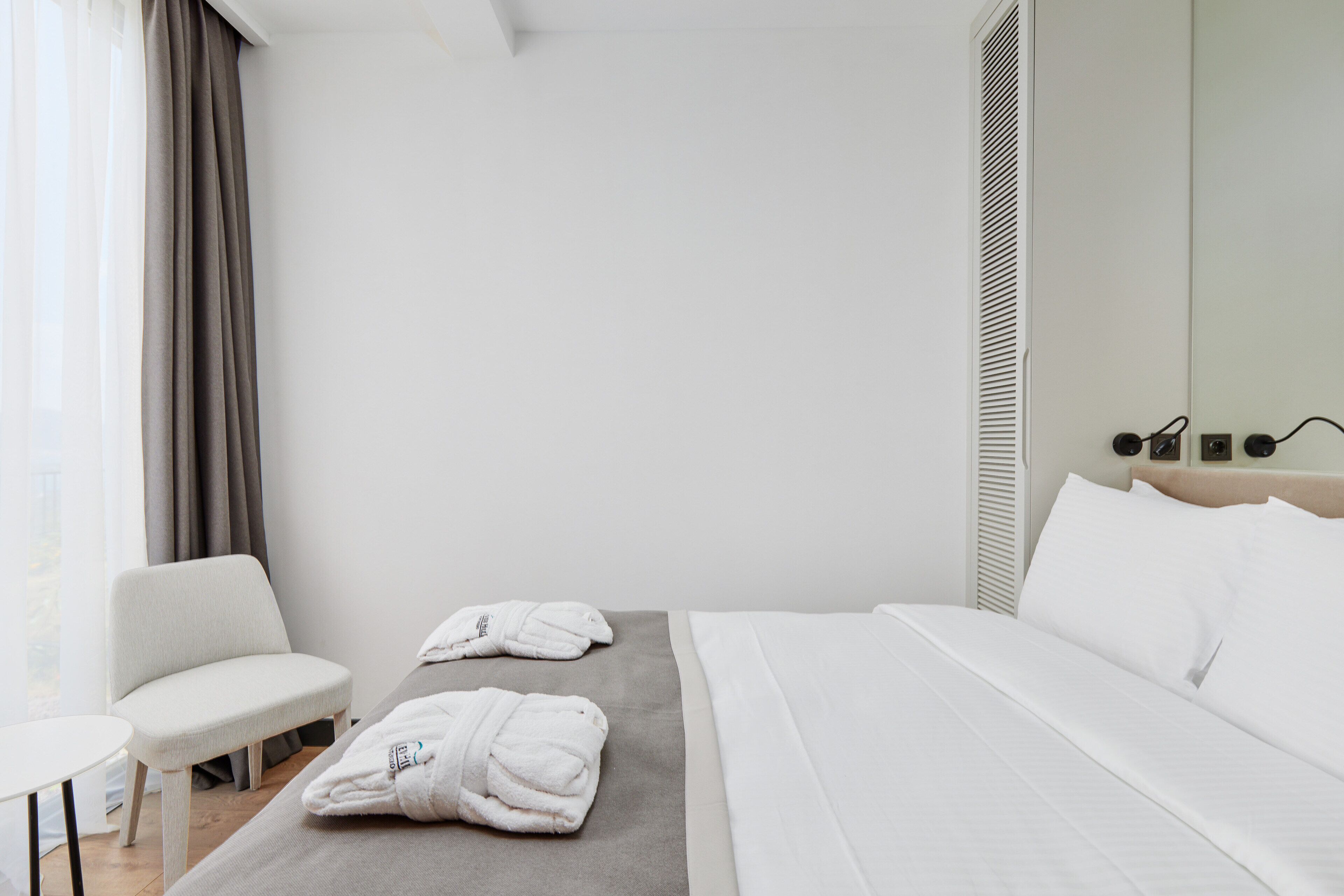 Habitació d'hotel amb un llit, una cadira i dues tovelloles sobre una taula.