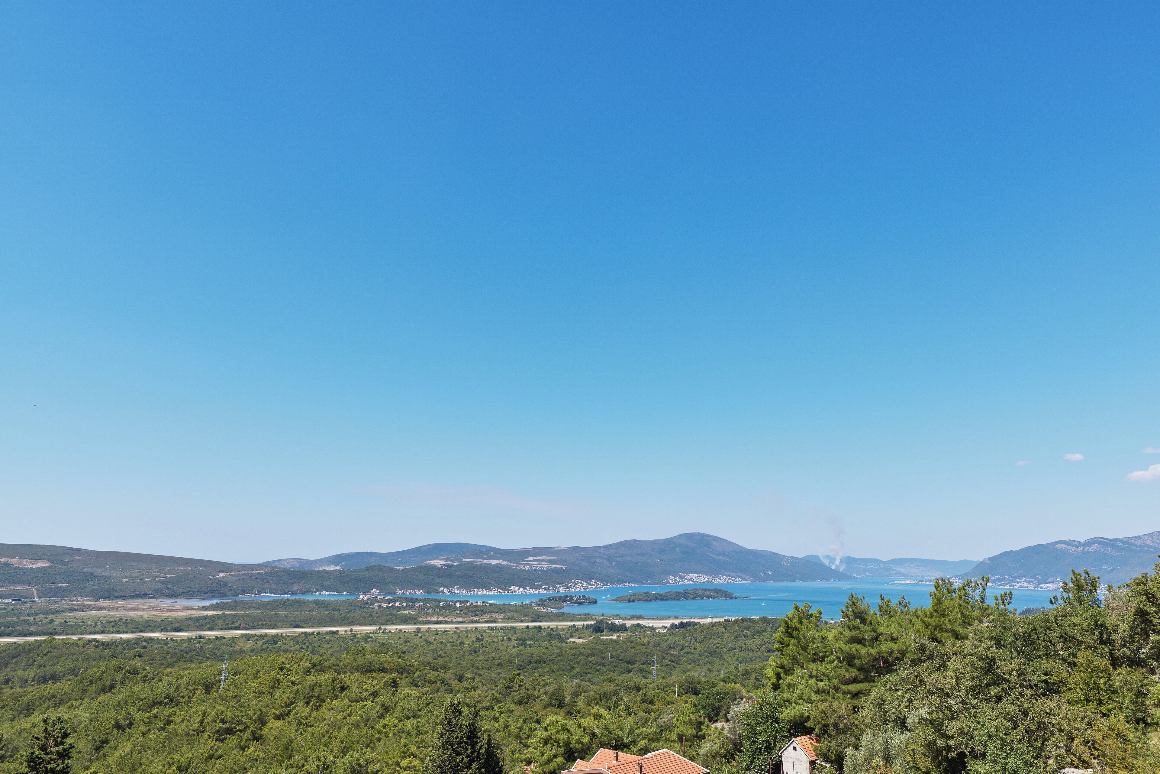 A coastal landscape with a clear view of the sea and distant mountains.