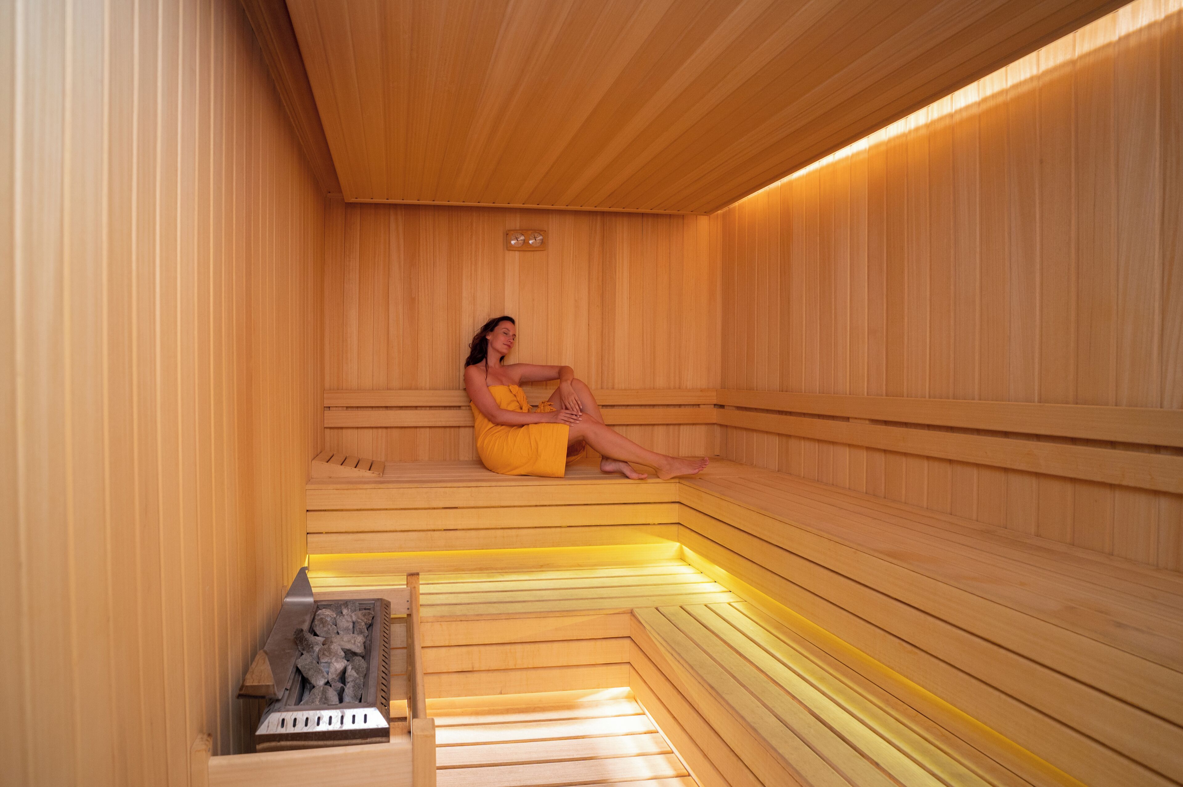 A sauna with wooden benches and a person sitting.