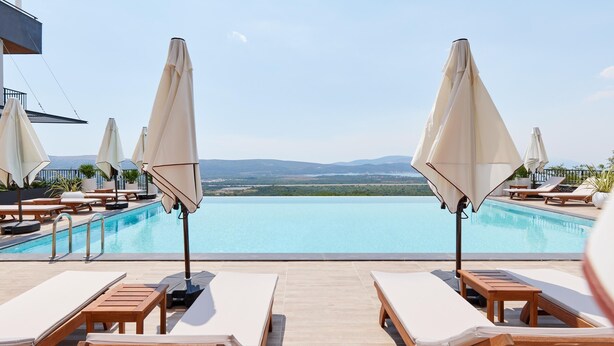 A poolside area with lounge chairs and umbrellas, overlooking a clear pool and distant landscape. - Bayview Hills Luxury Residences (Kotor)