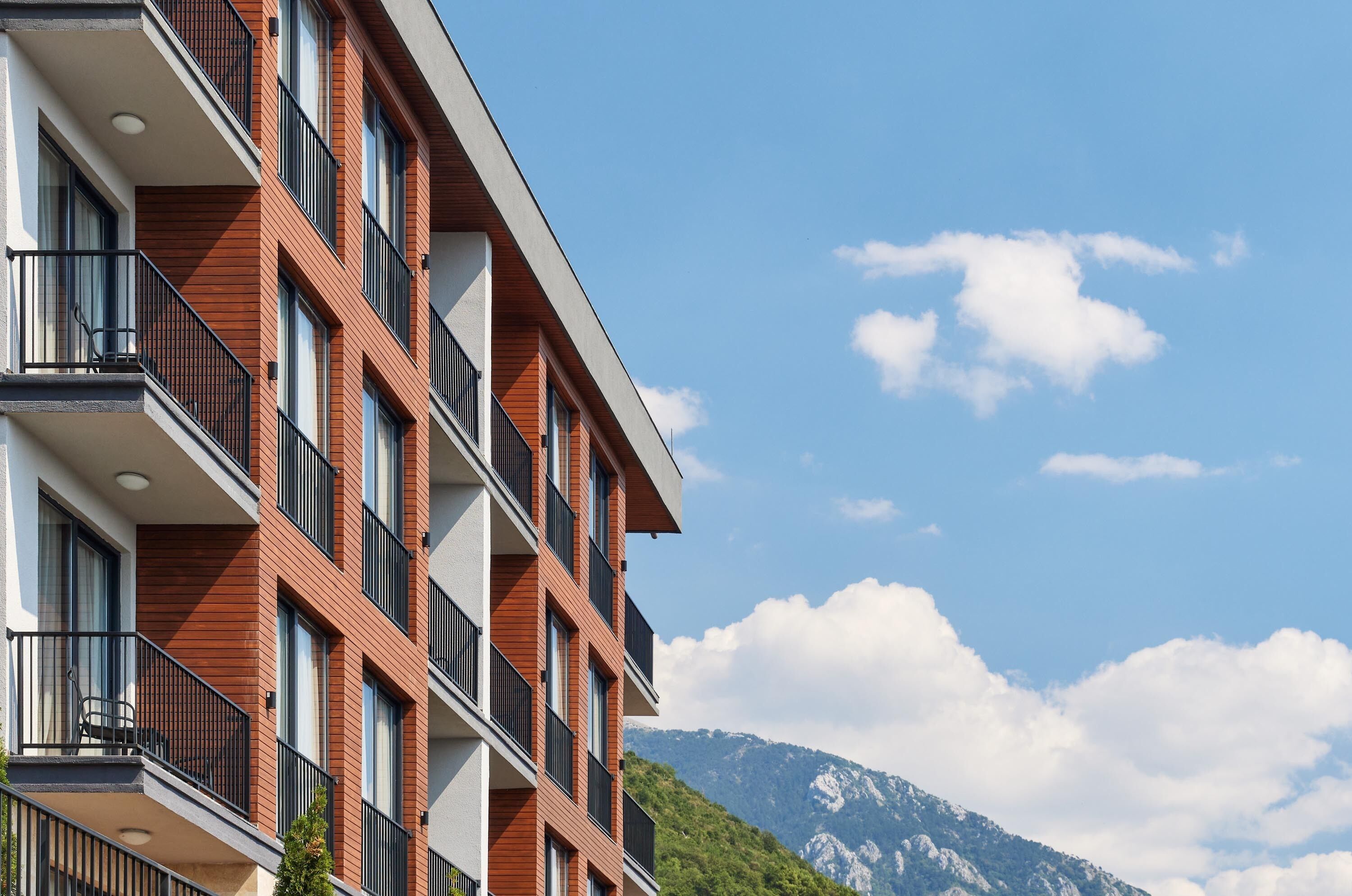 A multi-story building with balconies, large windows, and a mountainous backdrop.