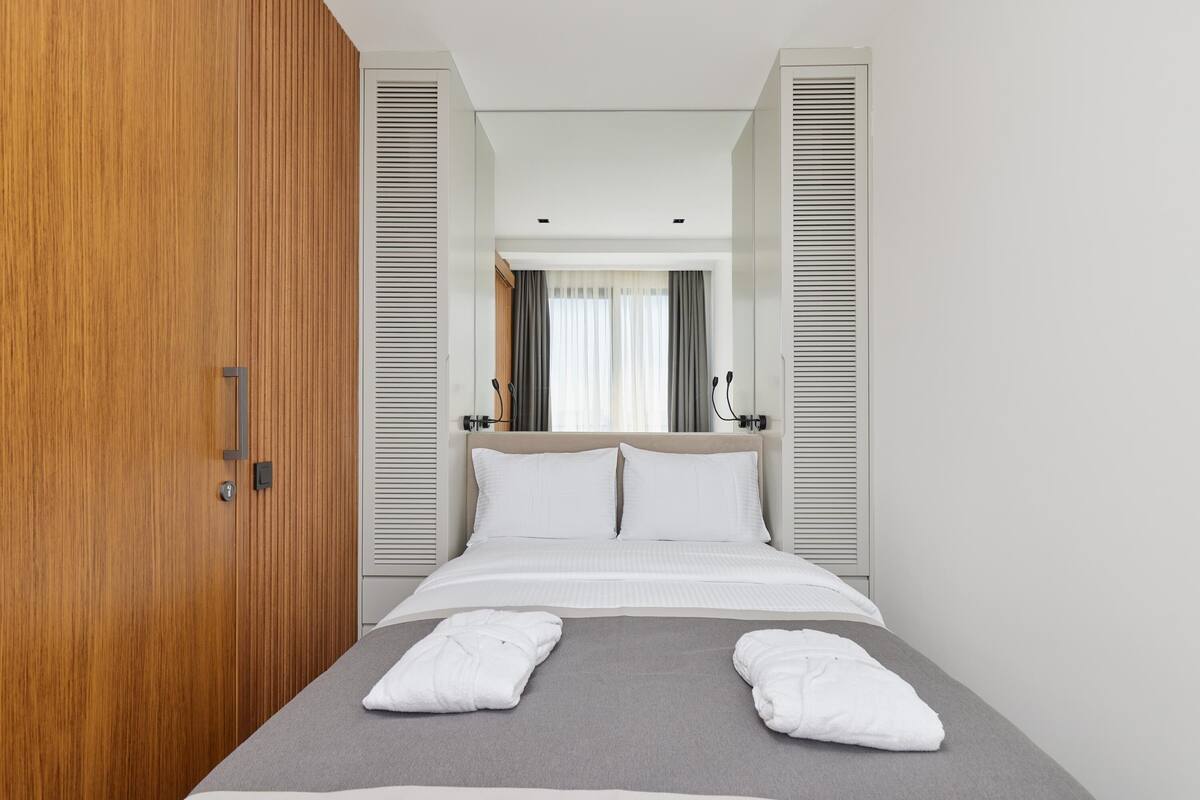 A modern hotel room with a bed, wooden wardrobe, and a view through a window with curtains.