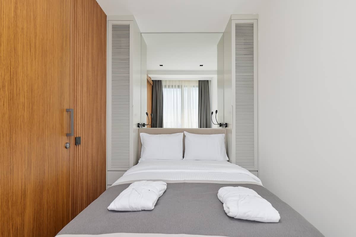 A modern hotel room with a bed, wooden wardrobe, and a view through a window with curtains.