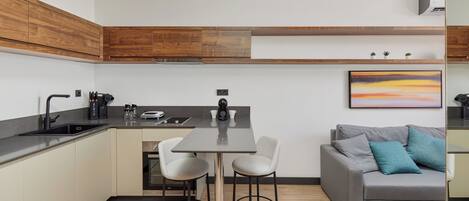 A modern kitchen with a dining area, wooden cabinets, a grey sofa with blue cushions, and a painting on the wall.