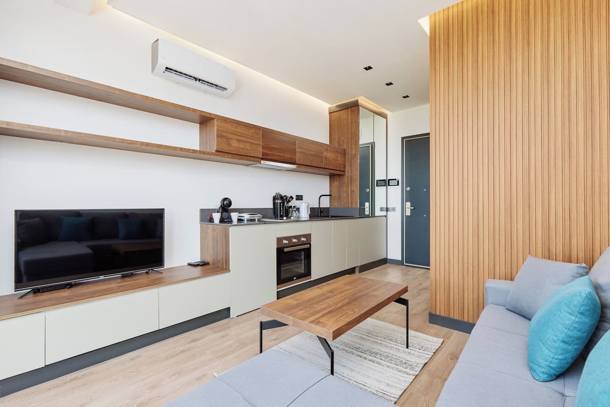 A modern living room with a flat-screen TV, wooden coffee table, and a sofa with cushions.