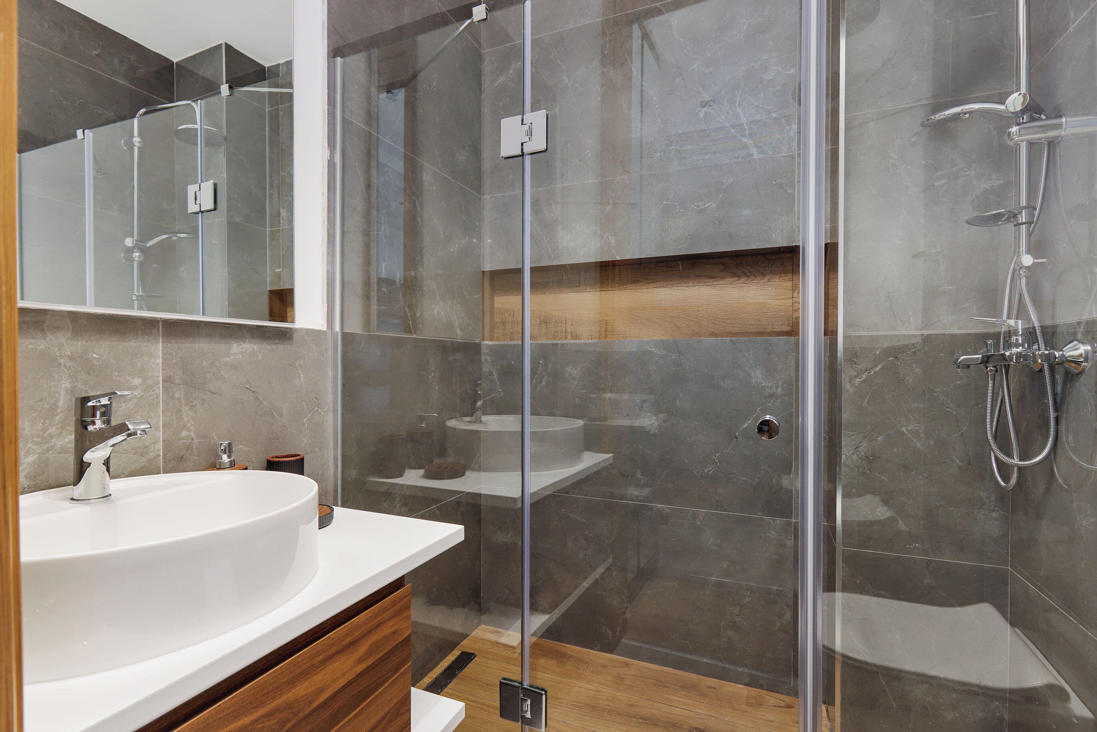 A modern bathroom with a glass-enclosed shower, a white sink, and a wooden vanity.