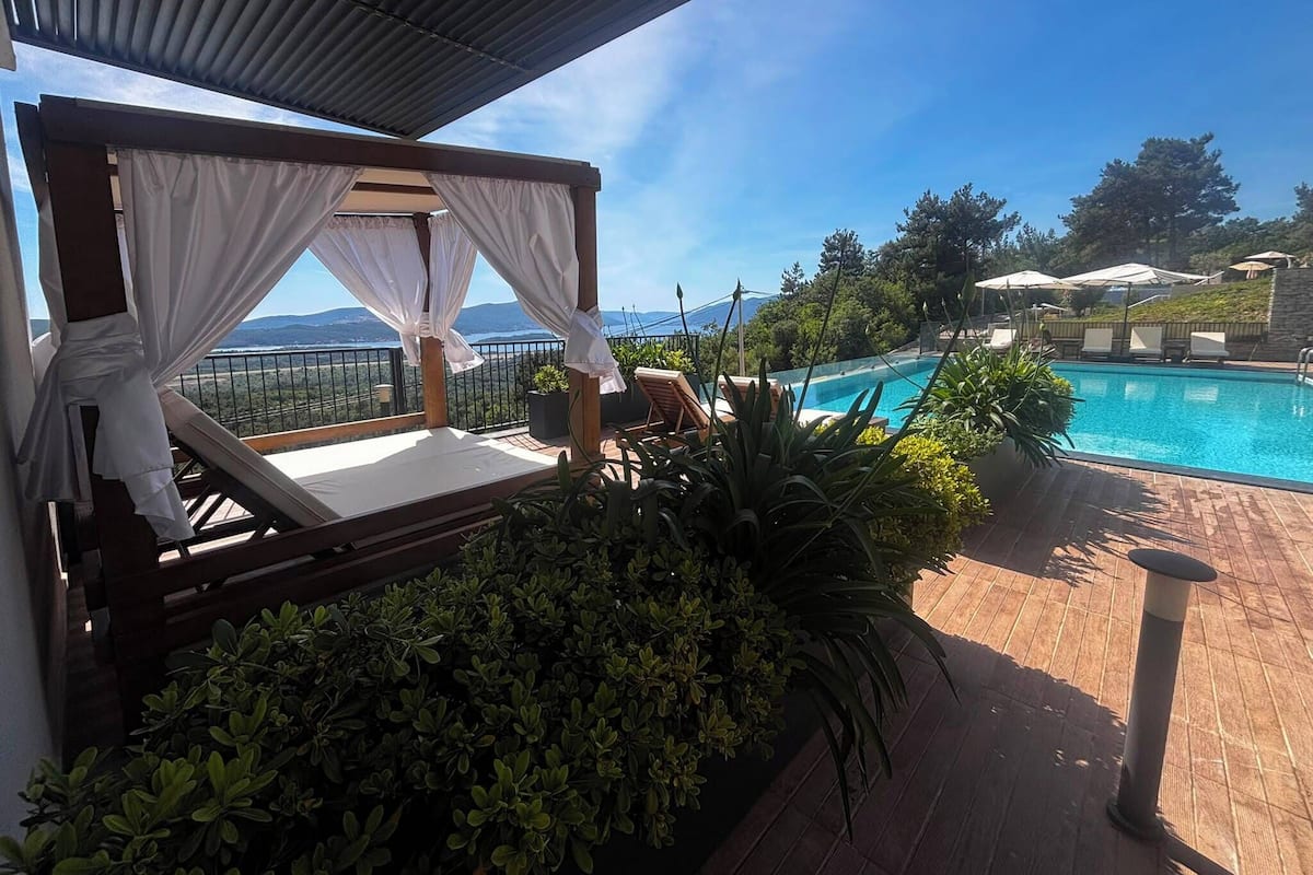 A balcony with a bed, a pool, and a view of the landscape.