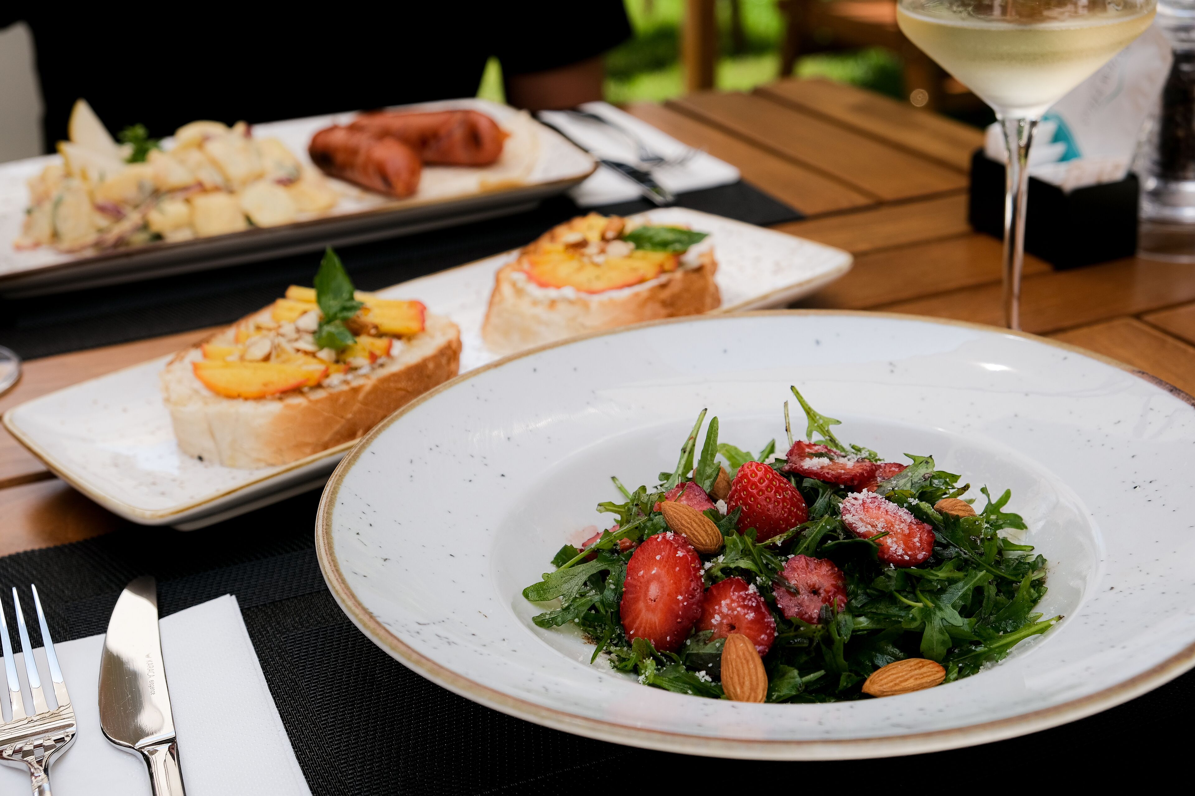 A dining table with a plate of salad, two plates of appetizers, and a glass of white wine.
