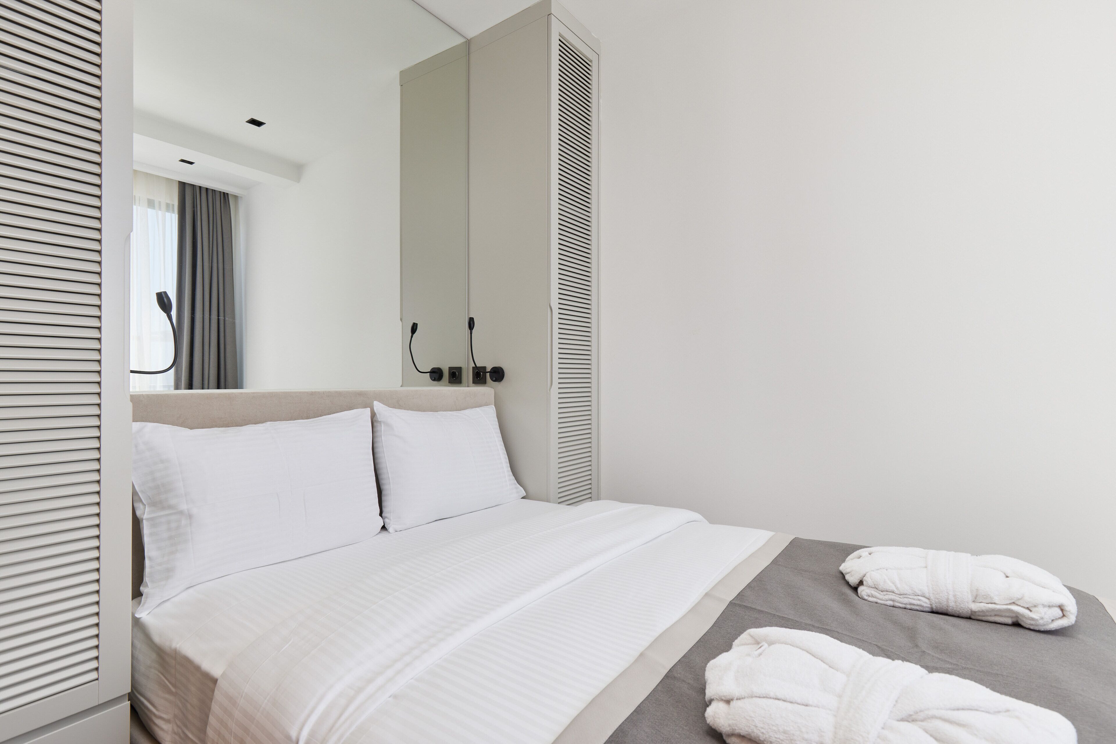 Une chambre d’hôtel moderne avec un grand lit, un miroir, une armoire et deux serviettes sur le lit.