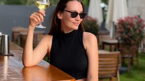 A person seated at an outdoor table with a glass of white wine, surrounded by wooden furniture and umbrellas. - Bayview Hills Luxury Residences (Kotor)