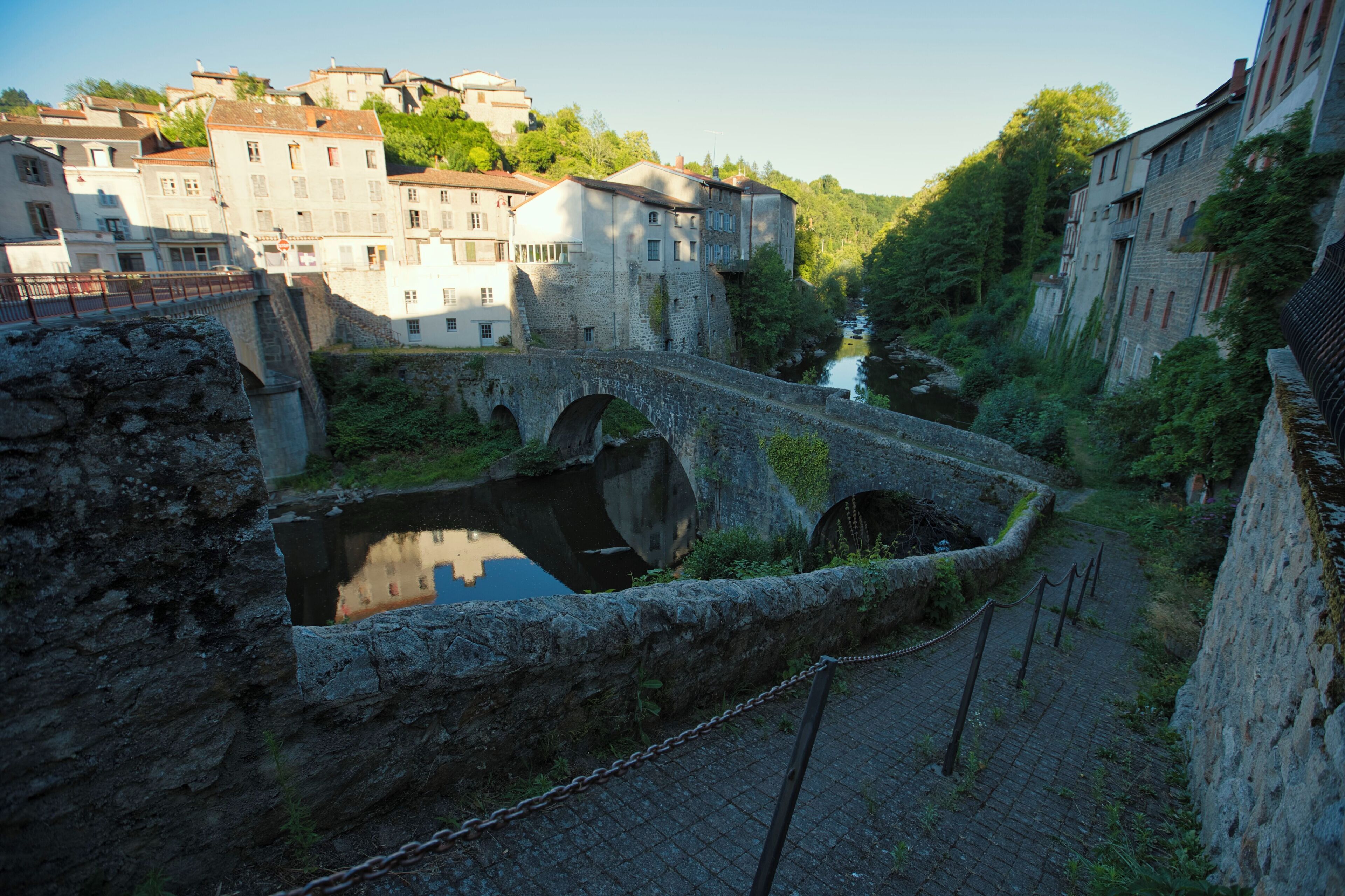 A historic stone bridge over a river, surrounded by old buildings and greenery.