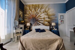 Habitación de hotel con una cama grande, un escritorio, una silla, un aparador y una pared con un mural decorativo.