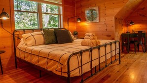Camera da letto in una accogliente baita di legno, con un letto a struttura in metallo, due lampade da comodino e vista sugli alberi attraverso ampie finestre.
